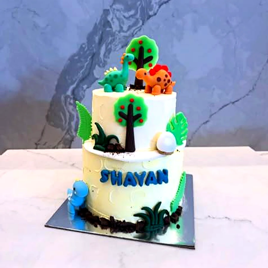 Two-tier dinosaur jungle cake with trees, leaves and a name in blue