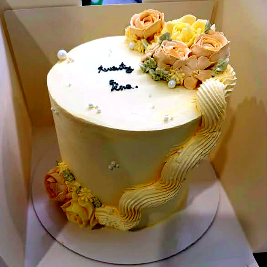Tall cream buttercream cake with piped peach roses and a wavy piped border